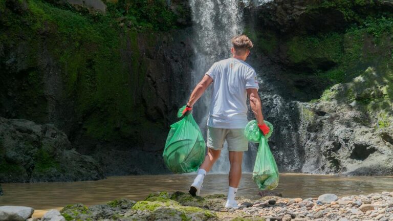 homem carregando sacolas com lixo proximo a uma cachoeira-min